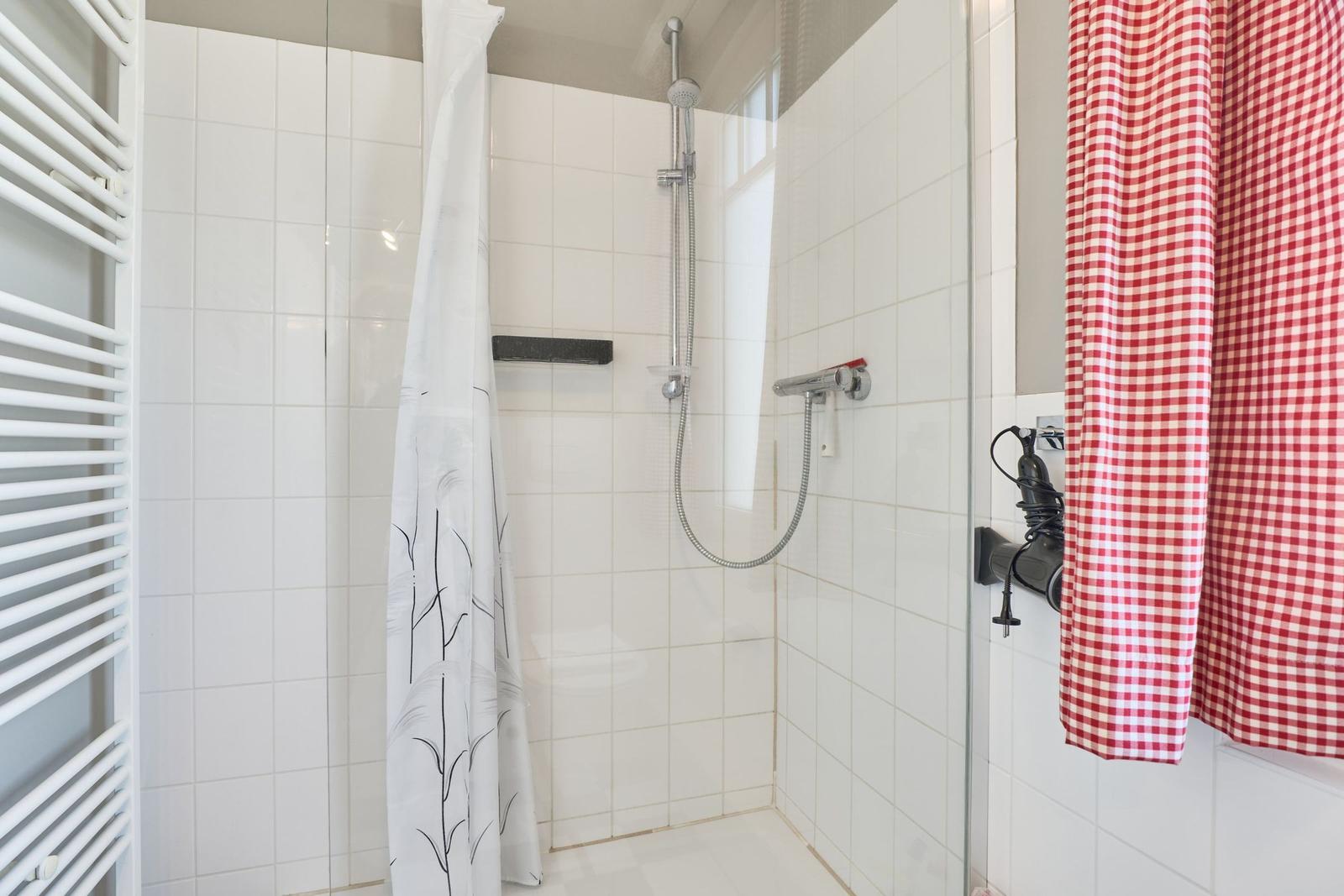 Dusche mit Duschbrause, weißen Fliesen und rotem kariertem Handtuch.