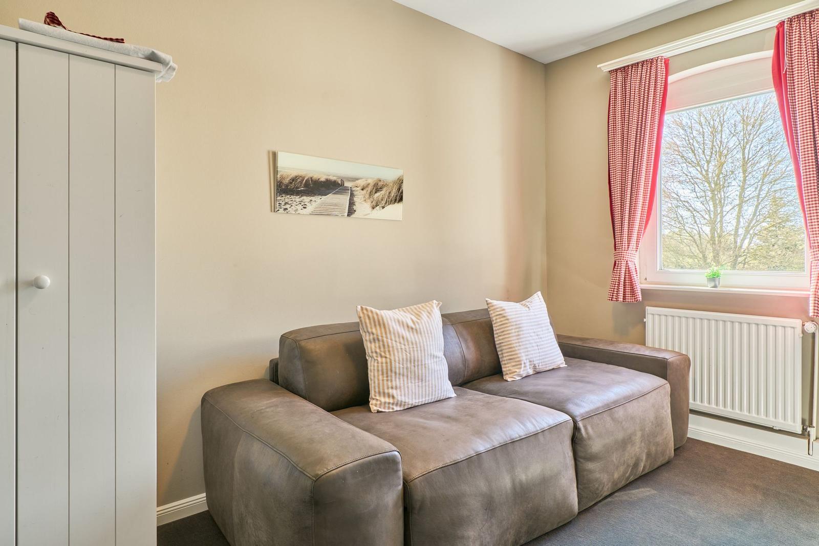 Ein Wohnzimmer mit braunem Sofa, weißen Kissen, einem weißen Schrank und einem Fenster mit roten Gardinen.