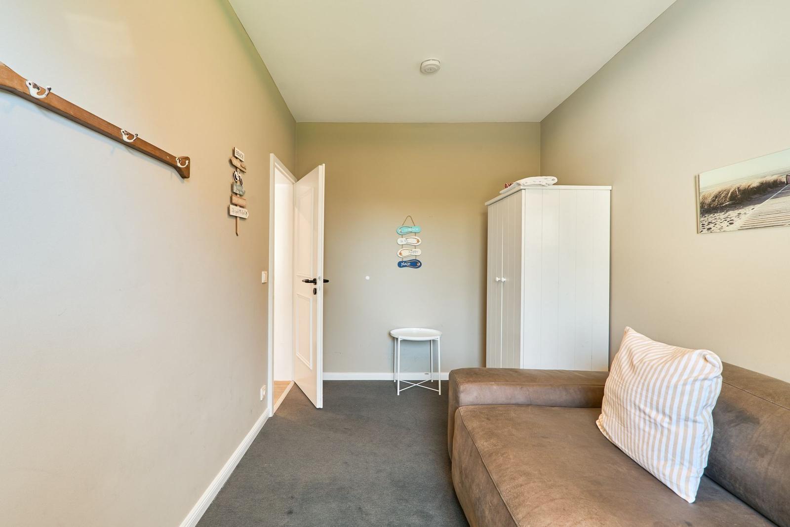 Wohnraum mit Sofa, Kleiderständer und Kleiderschrank. Tür führt in einen anderen Raum.