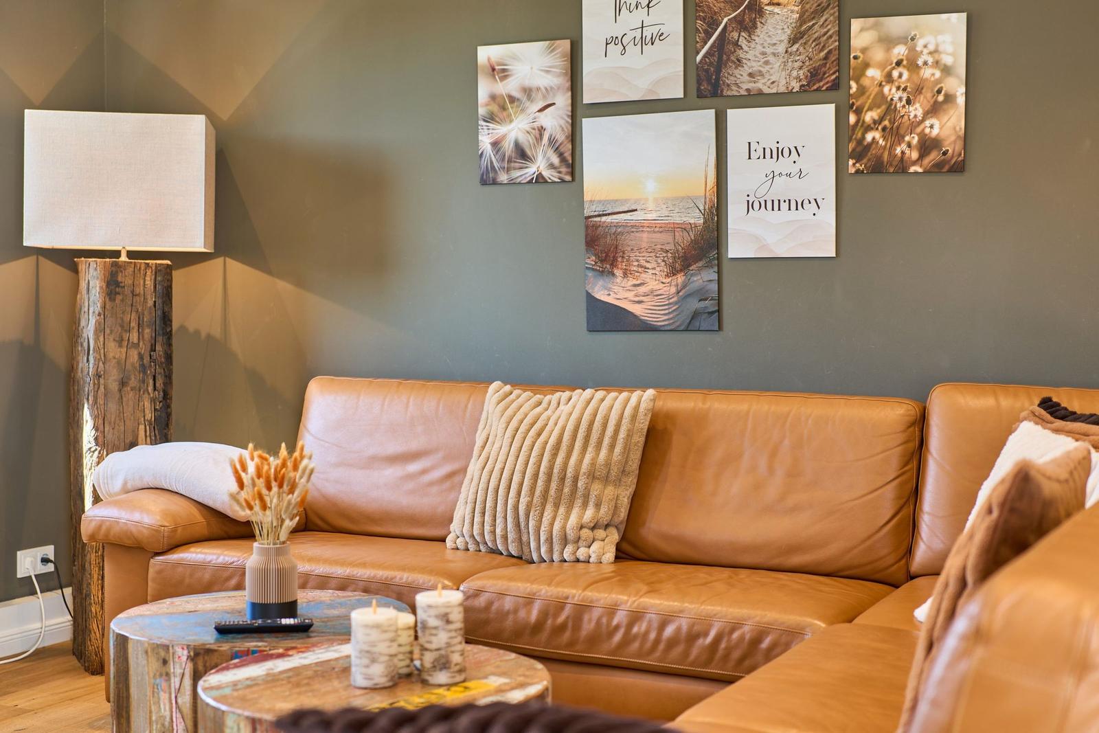 Ein braunes Ledersofa mit Kissen, Wandbilder und eine Stehlampe auf Holzsockel.