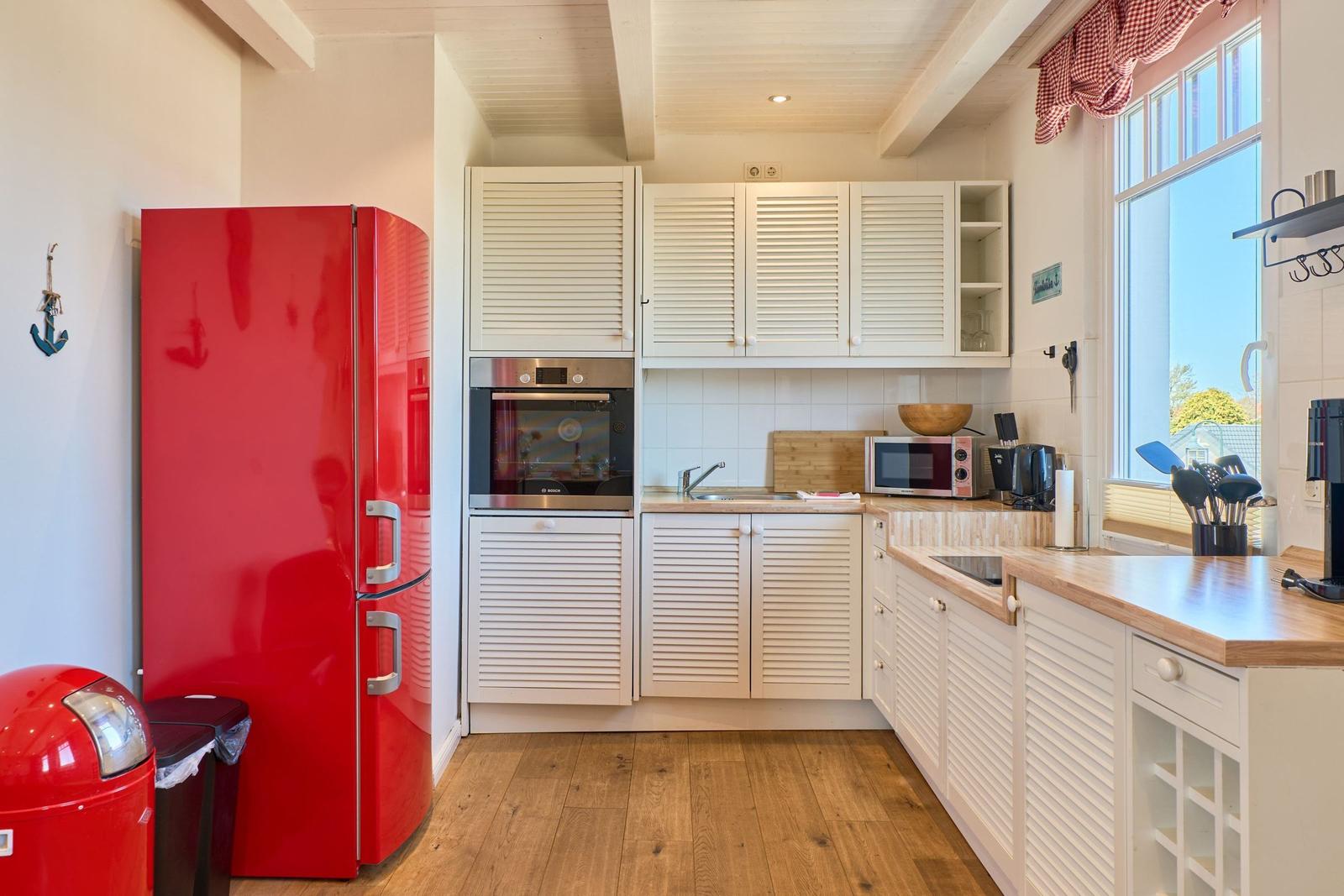 Küche mit rotem Kühlschrank, weißen Schränken und Holzoberflächen.