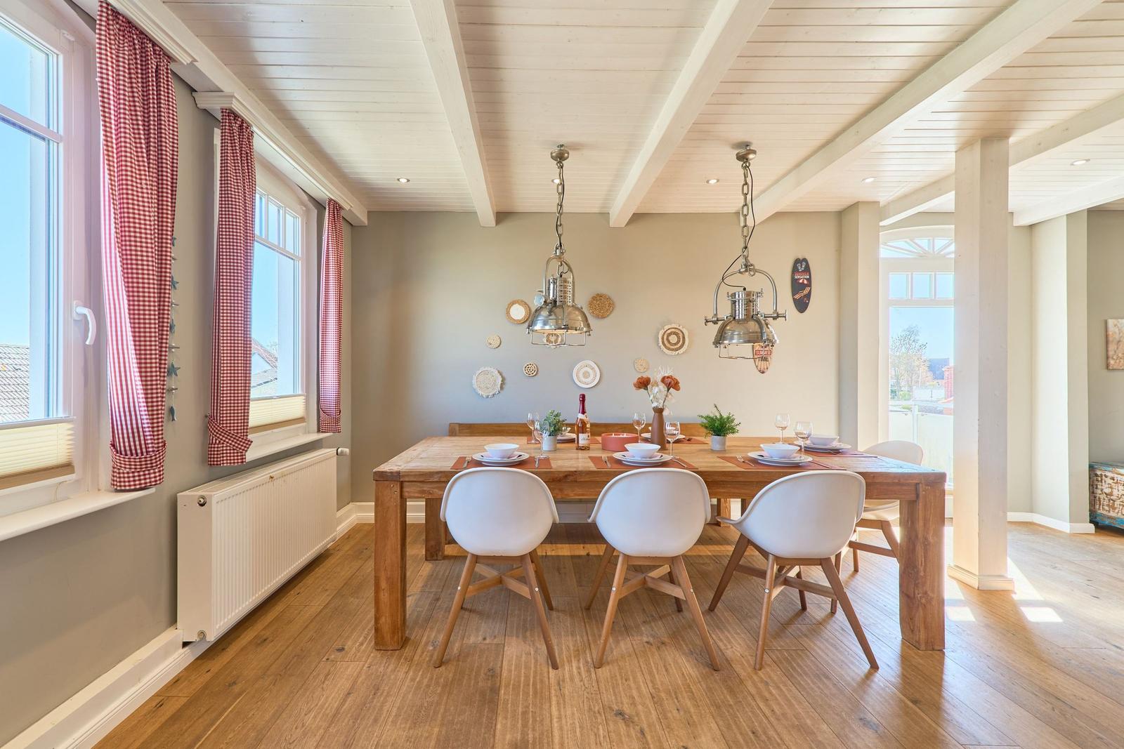 Esszimmer mit Holztisch, weißen Stühlen und roten Gardinen an den Fenstern.