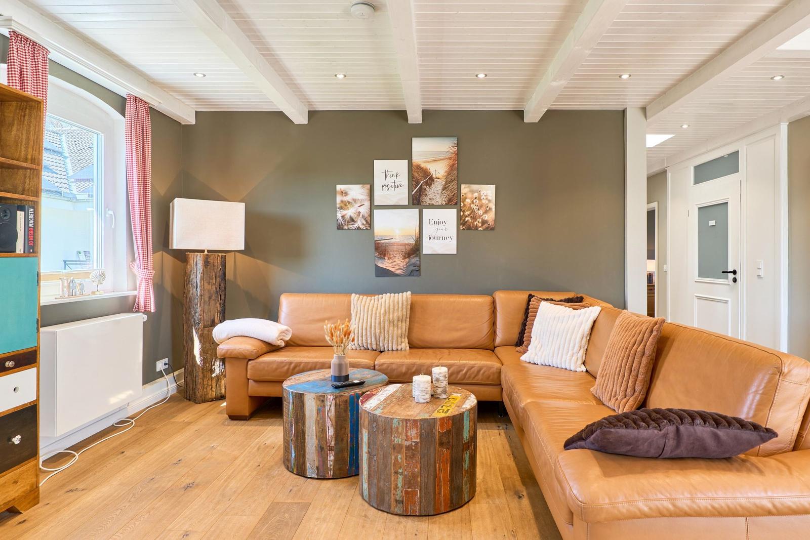 Wohnzimmer mit braunem Sofa, Holztischen und Wandbildern.