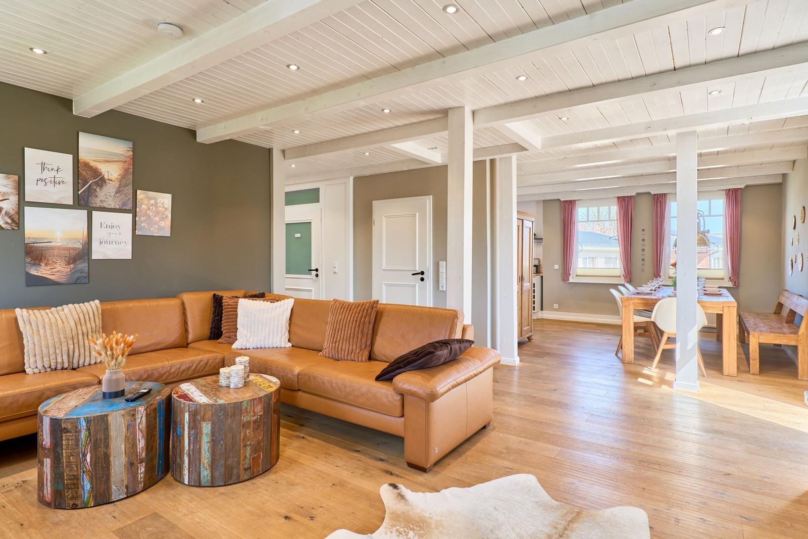Wohn- und Essbereich mit braunem Sofa, Holzboden und Deckenbalken.