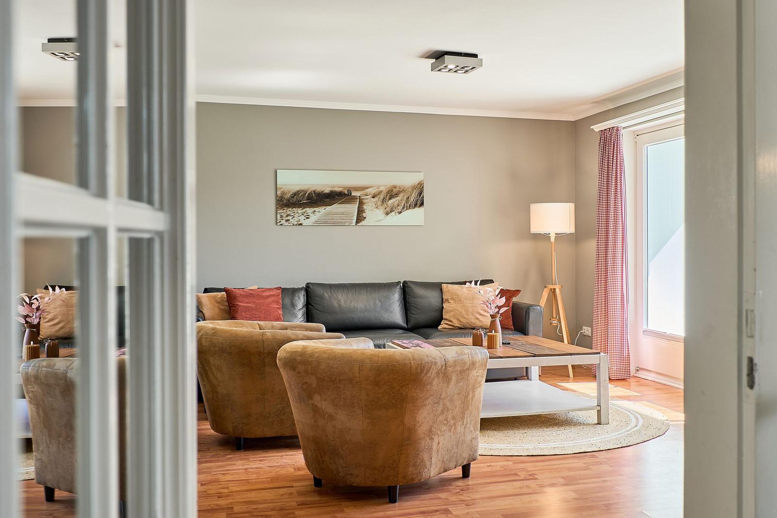 Wohnzimmer mit Sofa, zwei Sesseln, Tisch und Wandbild.