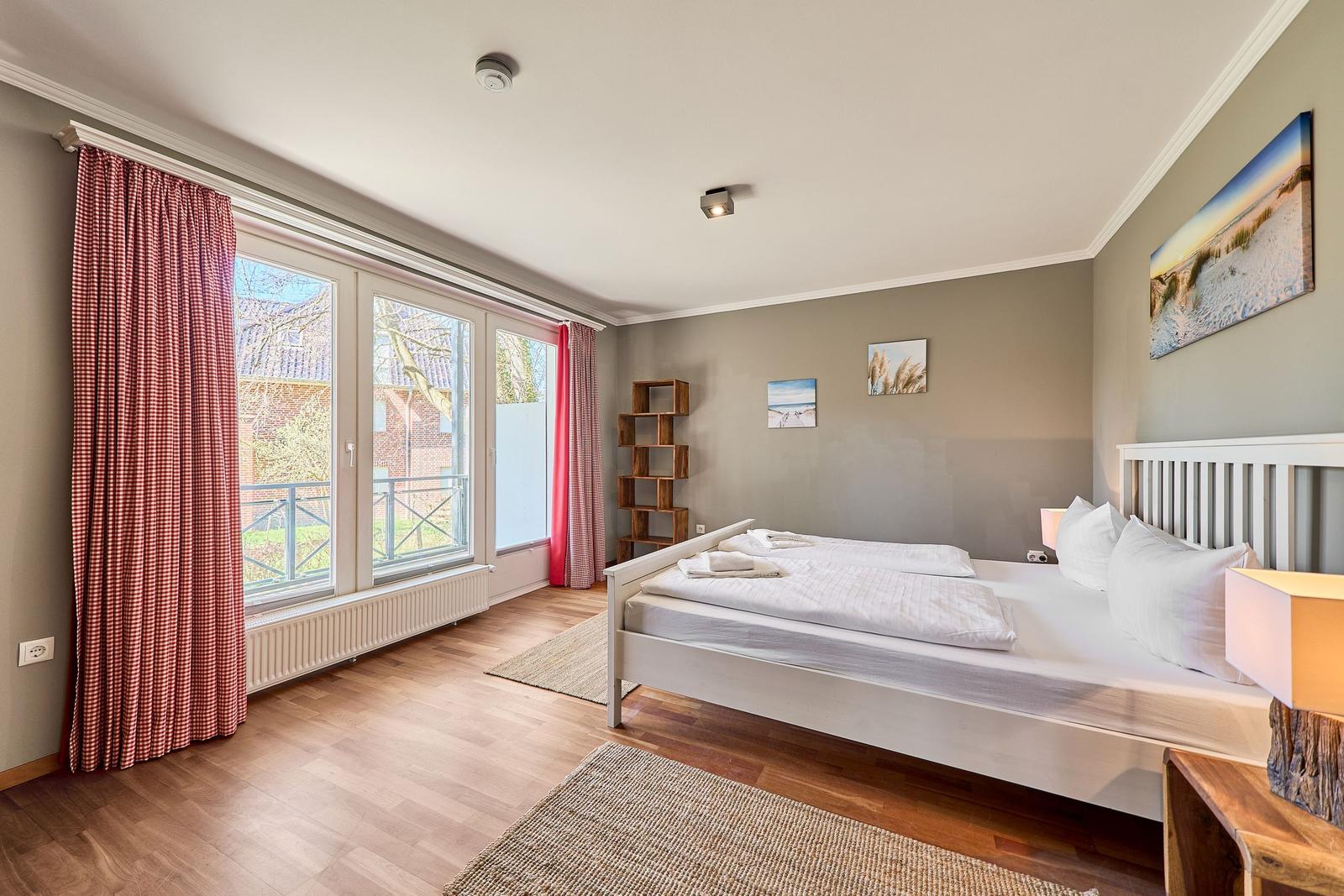 Schlafzimmer mit Doppelbett, Holzboden und großem Fenster mit Blick auf Garten.