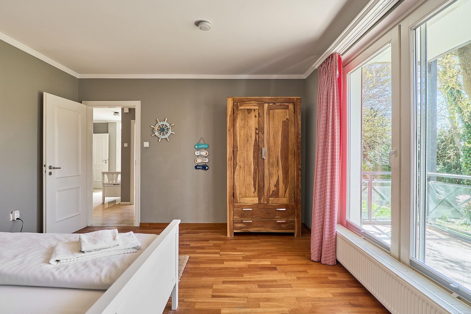 Schlafzimmer mit Holzboden, großer Garderobe und Blick auf Balkon.