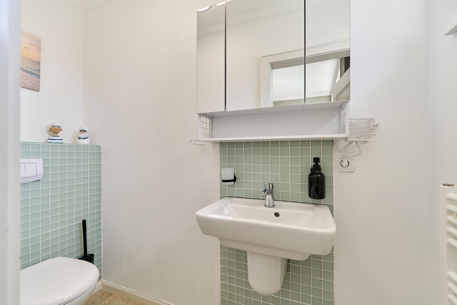 Badezimmer mit Waschbecken, Spiegelschrank und Toilette. Wandfliesen in mintfarben.