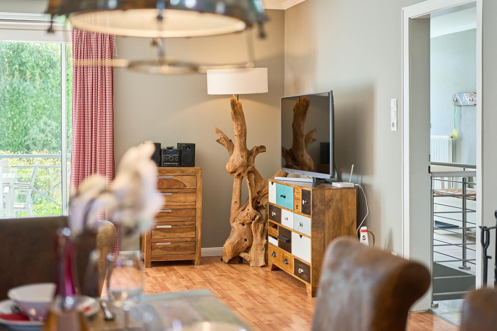 Wohnzimmer mit Holzmöbeln, Fernseher und Blick auf Balkon.