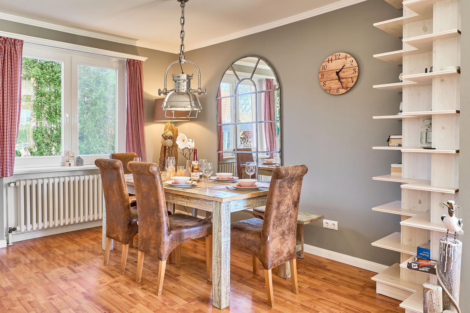 Esszimmer mit Holztisch, Lederstühlen, Spiegel und Bücherregal.