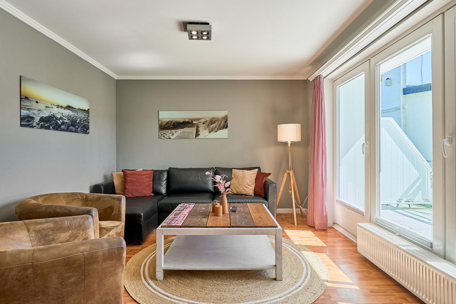 Wohnzimmer mit Sofa, zwei Sesseln, Tisch und Fenster zur Terrasse.