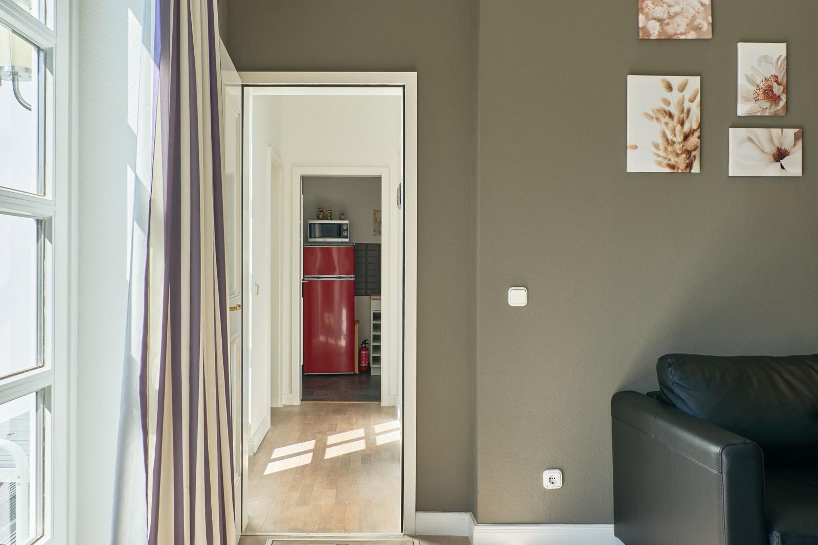 Wohnbereich mit Blick in die Küche. Roter Kühlschrank und Wandbilder sichtbar.