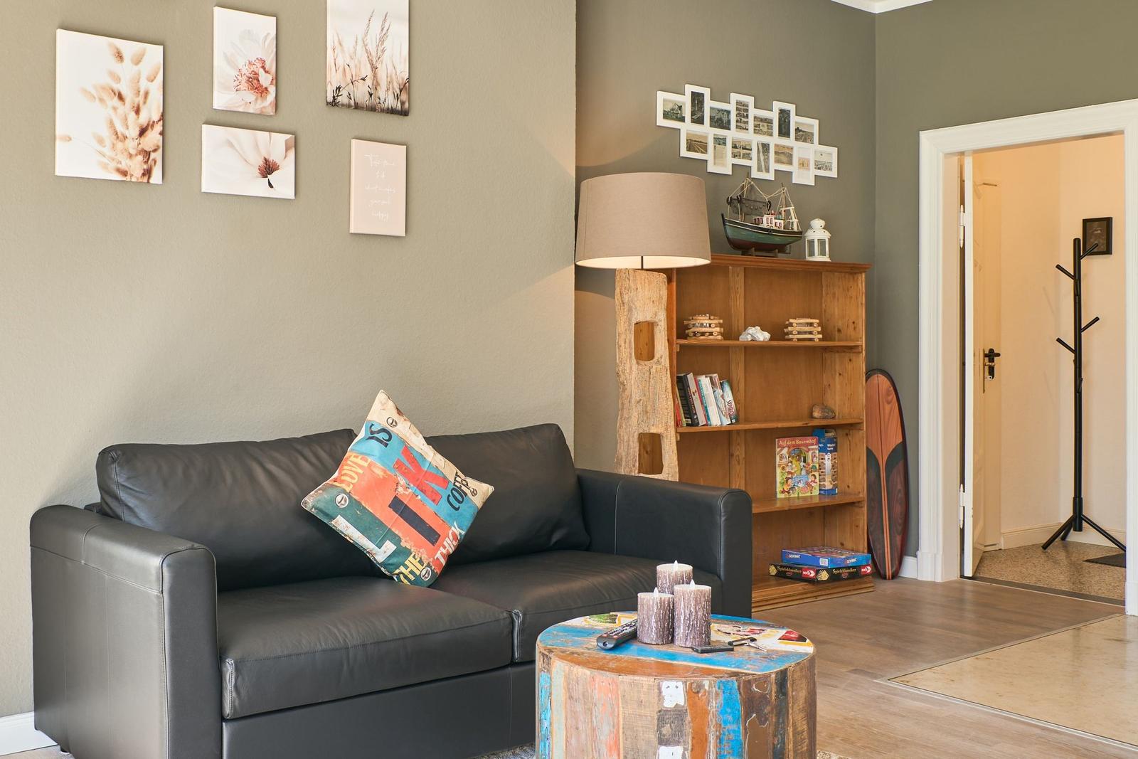 Ein Wohnzimmer mit Sofa, Couchtisch und Bücherregal. Wanddekoration und Tür sichtbar.