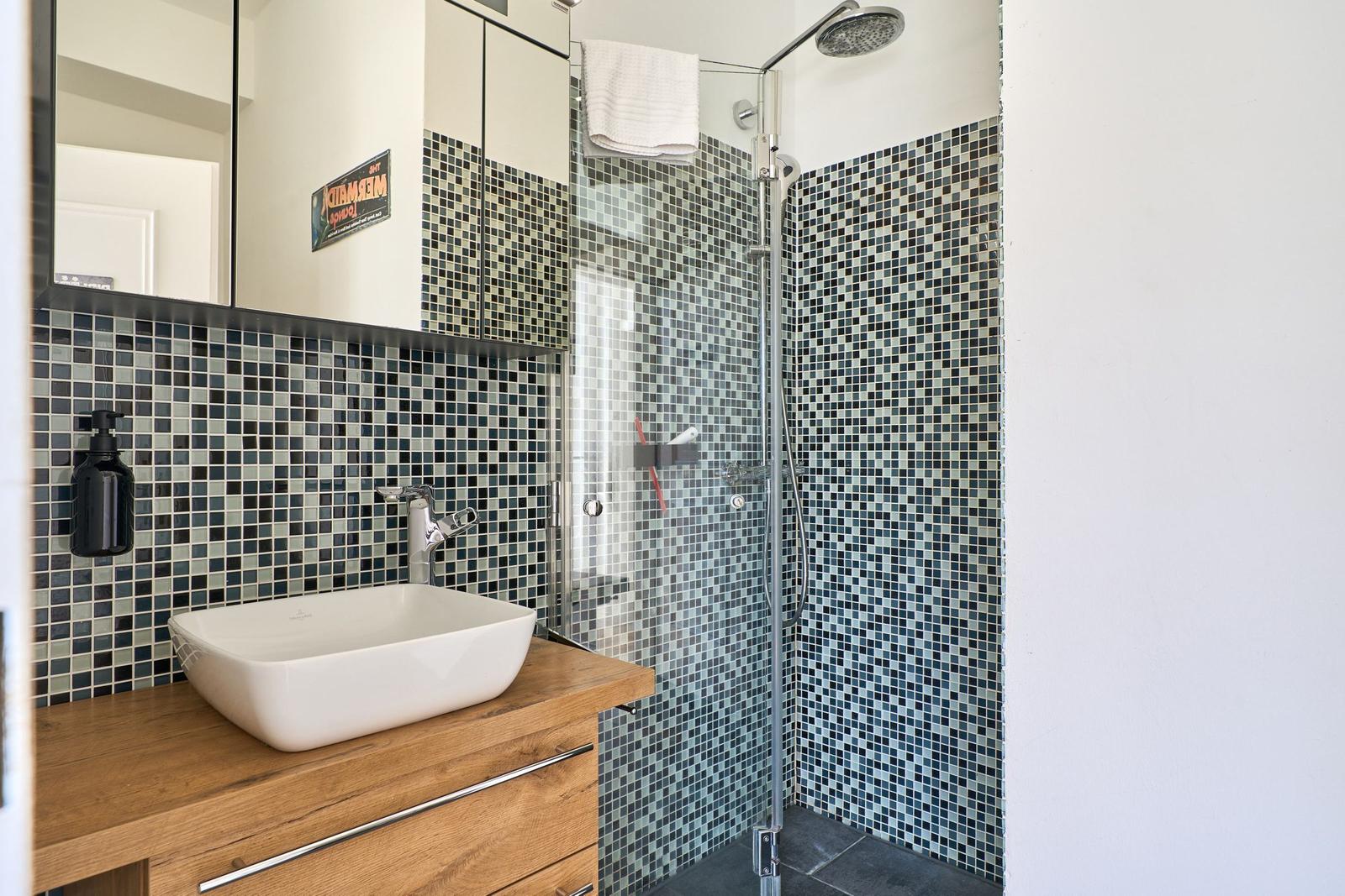 Bad mit Dusche und Waschbecken auf Holzunterlage.