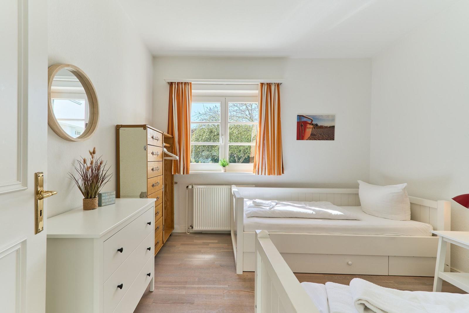 Schlafzimmer mit zwei Betten, Fenster, Gardinen und Schminktisch.