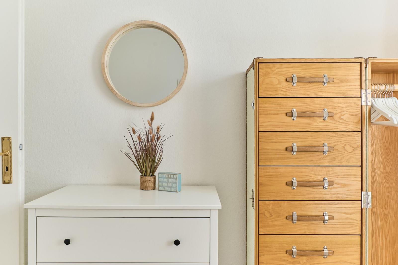 Schrank mit Schubladen und Spiegelform, weiße Kommode mit Pflanze.