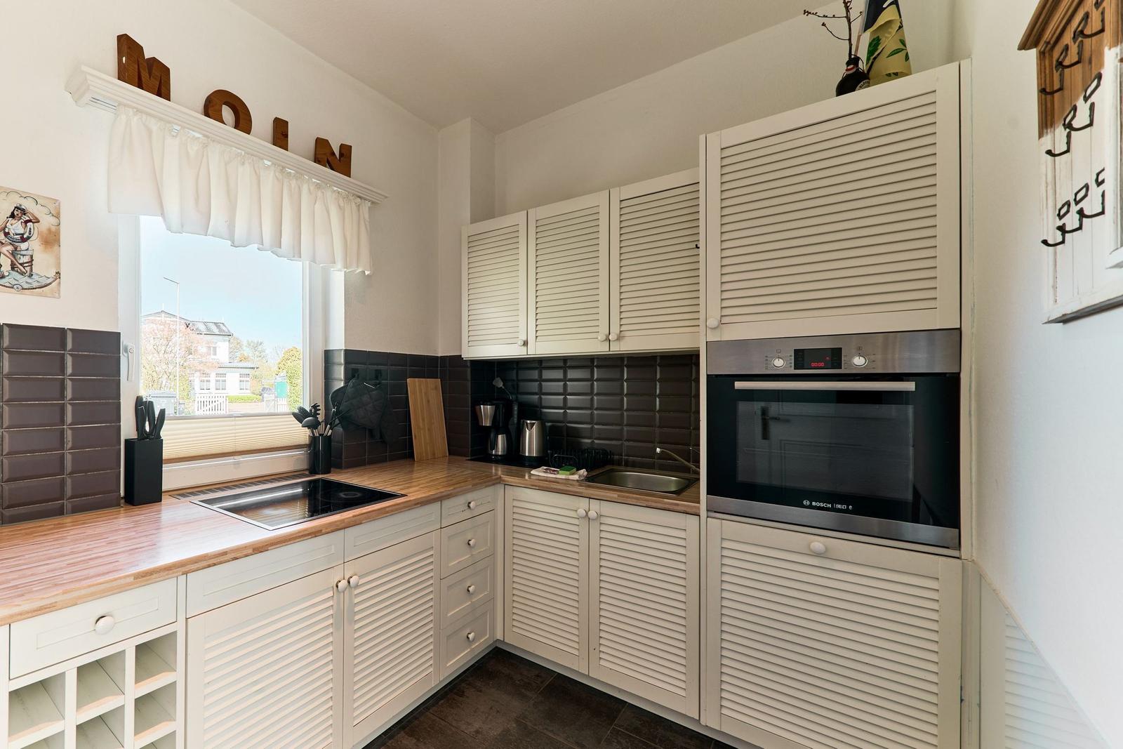 Küche mit weißen Schränken, Holzoberfläche und integriertem Backofen.