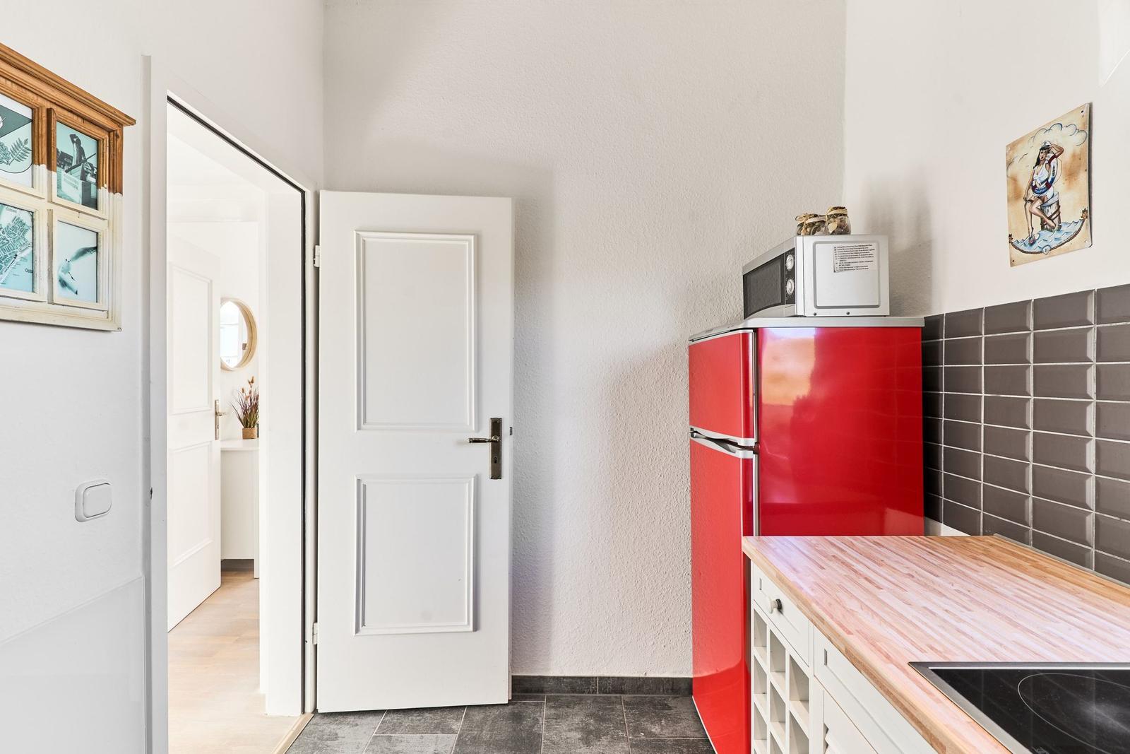 Küche mit rotem Kühlschrank, Holzplatte und Mikrowelle. Tür führt in angrenzenden Raum.