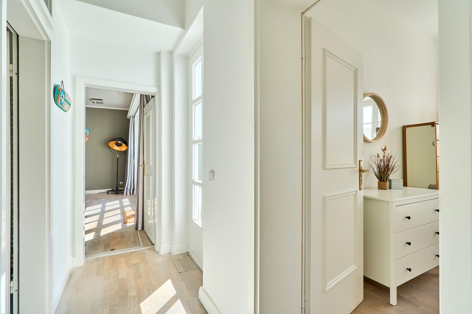 Flur mit weißer Tür und Schrank. Durchgang zu einem Raum mit Lampe und Vorhängen.