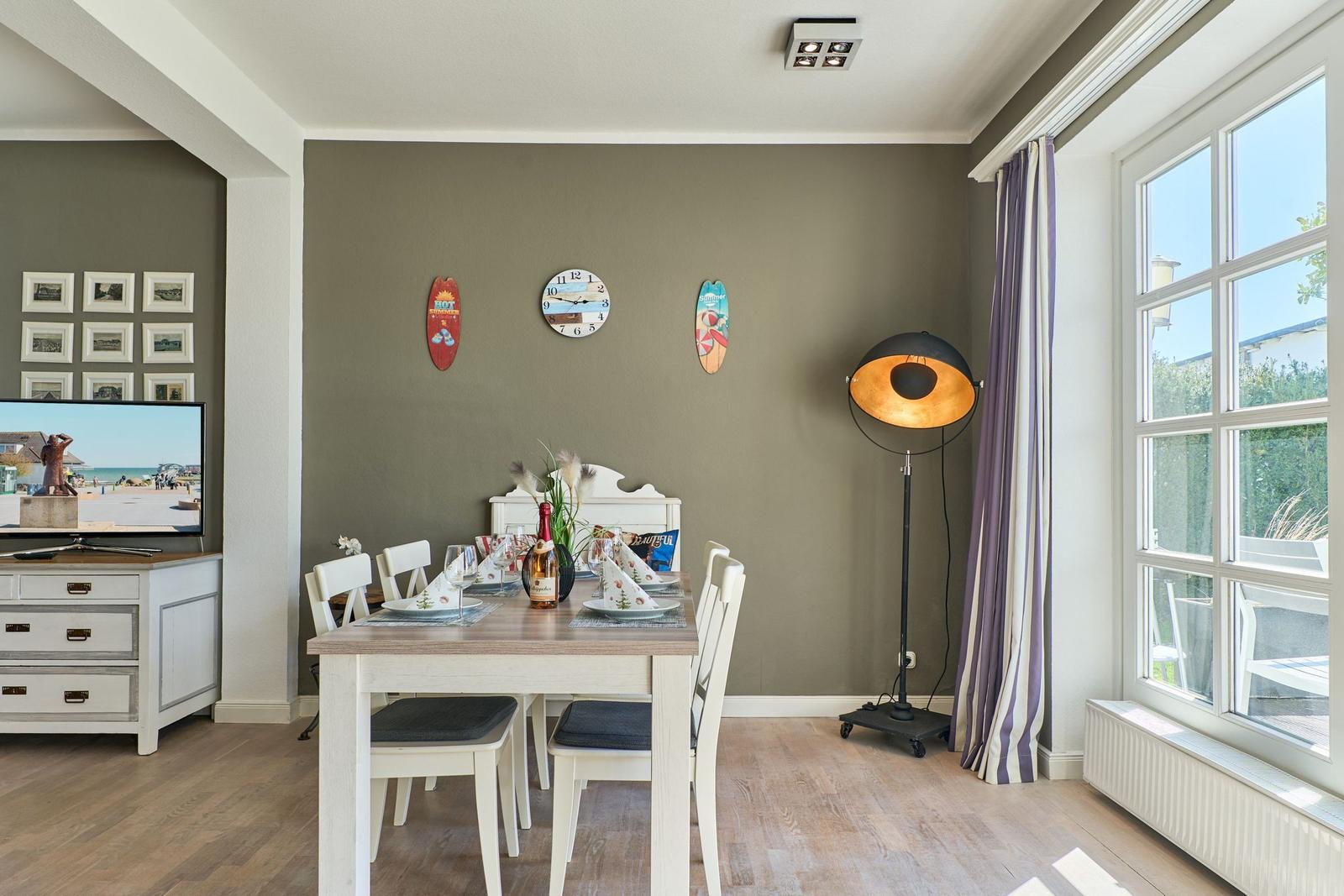 Essbereich mit Tisch, Stühlen und Fenster. Wanduhr und Dekorationen an der Wand.