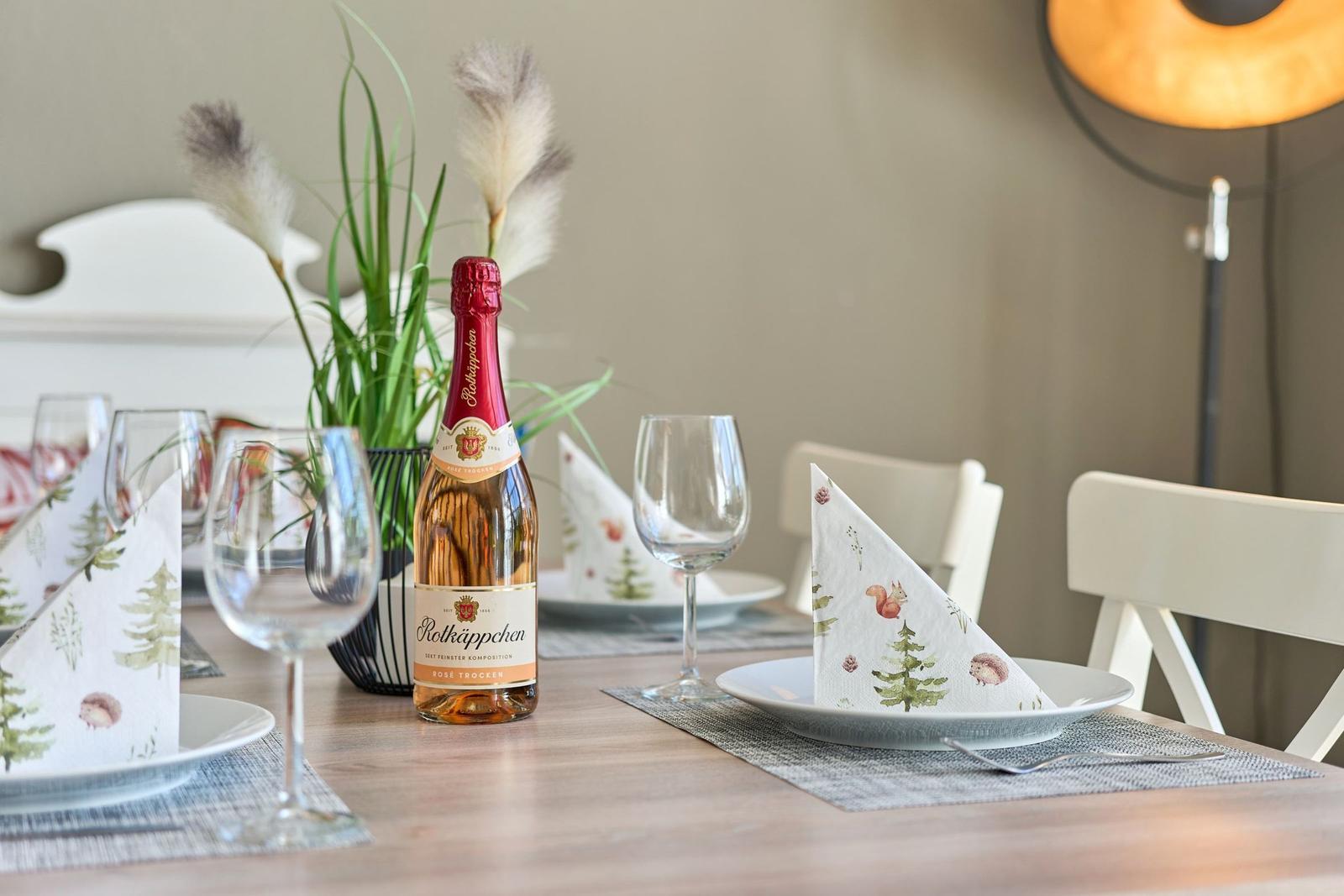 Gedeckter Tisch mit Flasche Rotkäppchen, Gläsern und Tischsets mit Tiermotiven.