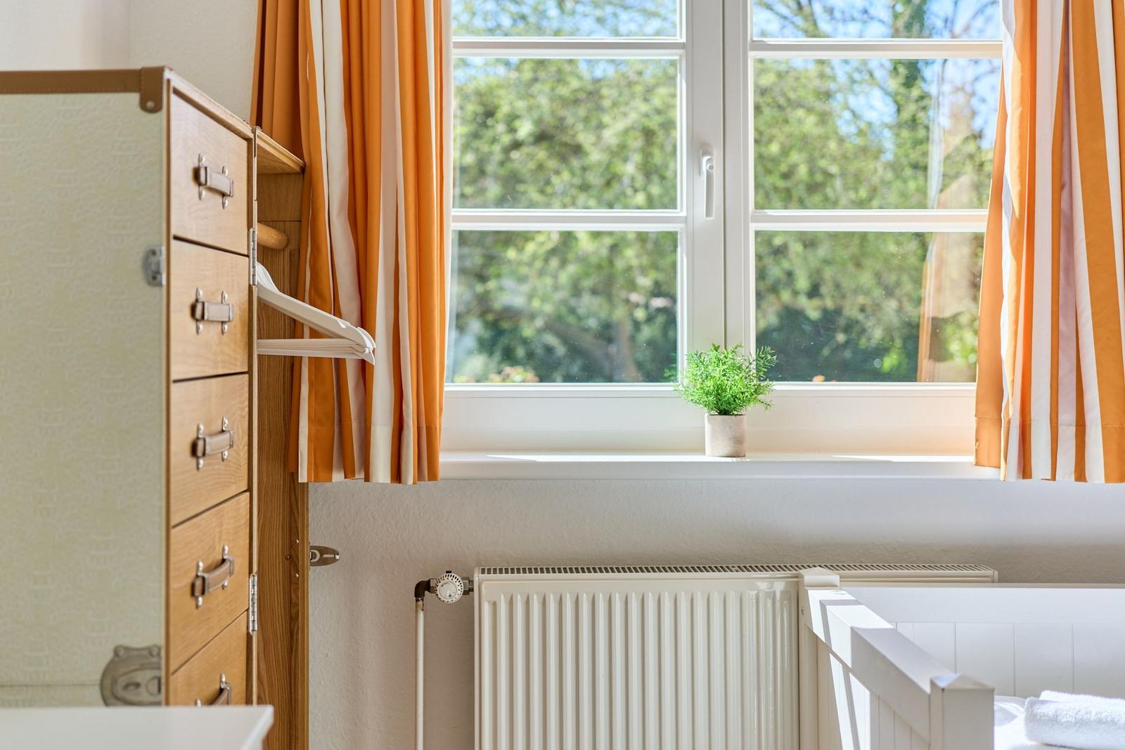 Ein Raum mit Fenster, Vorhängen, Heizkörper und Kinderbett.