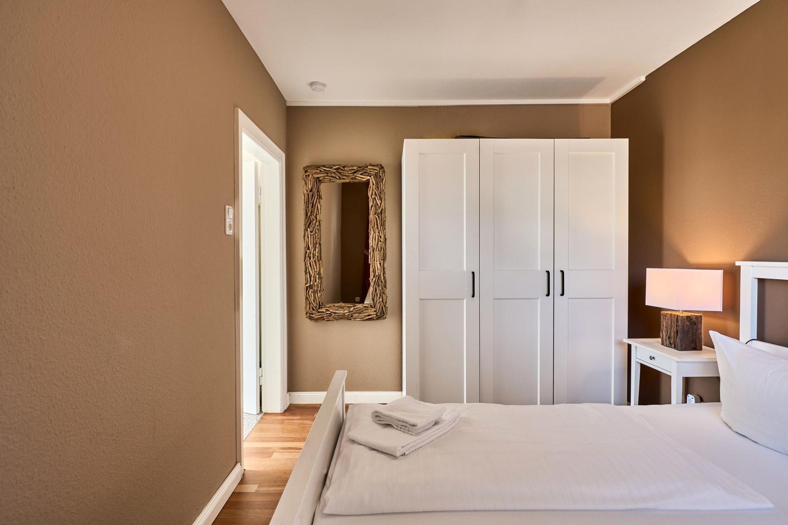 Schlafzimmer mit Bett, Kleiderschrank und Spiegel an der Wand.