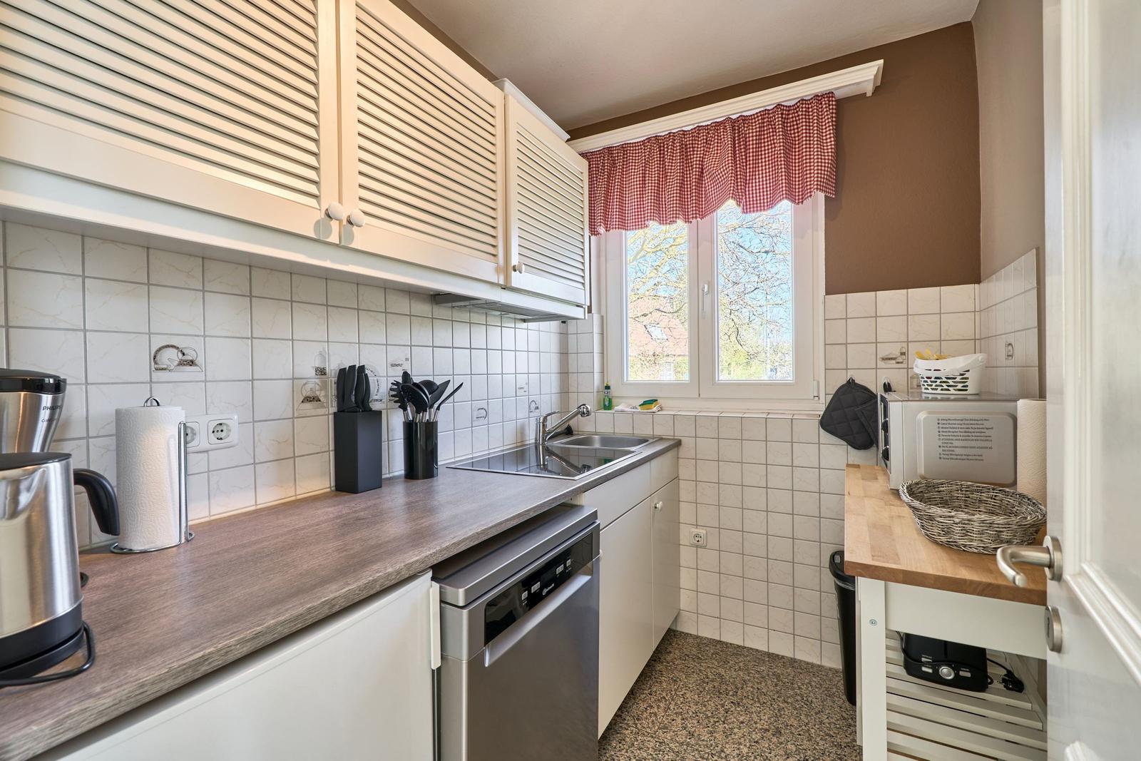 Küche mit Spüle, Dunstabzug, Kühlschrank und Fenster mit rotem Vorhang.