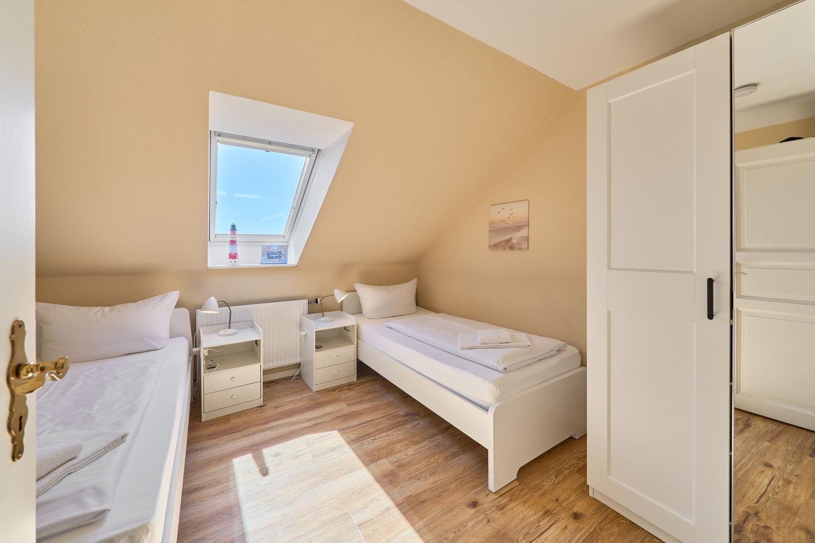 Zimmer mit zwei Betten, Dachschrägen, Fenster und Schrank.