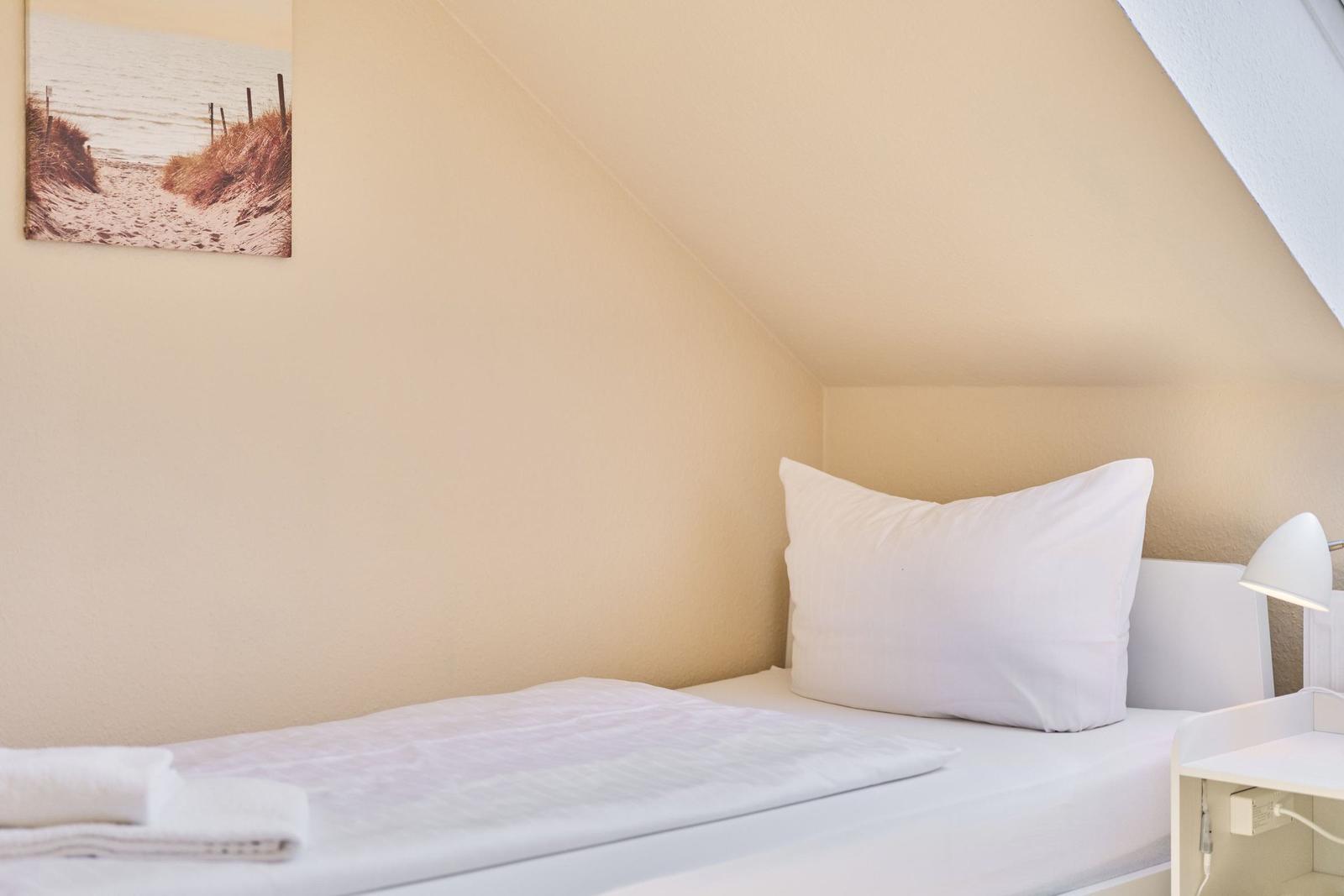 Schlafzimmer mit Bett, Kissen und Wandbild an geneigter Decke.