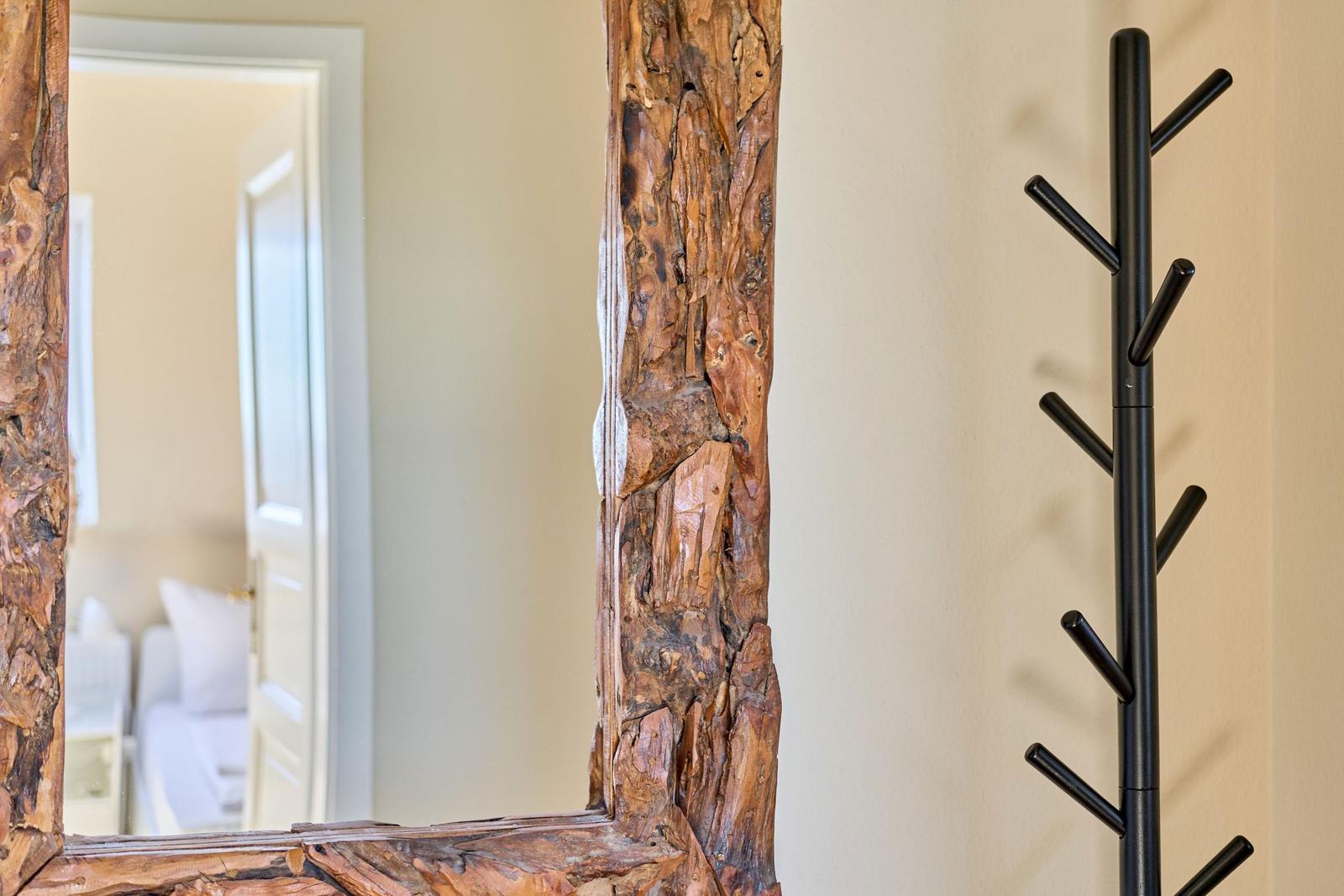 Spiegel mit rustikalem Holzrahmen und schwarzer Garderobe an der Wand.