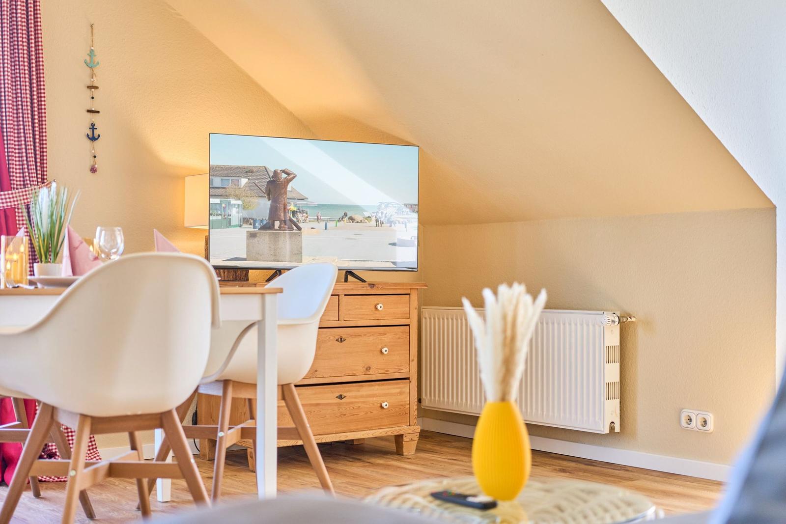 Ein Wohnzimmer mit TV, Esstisch und Holzmöbel unter einer Dachschräge.