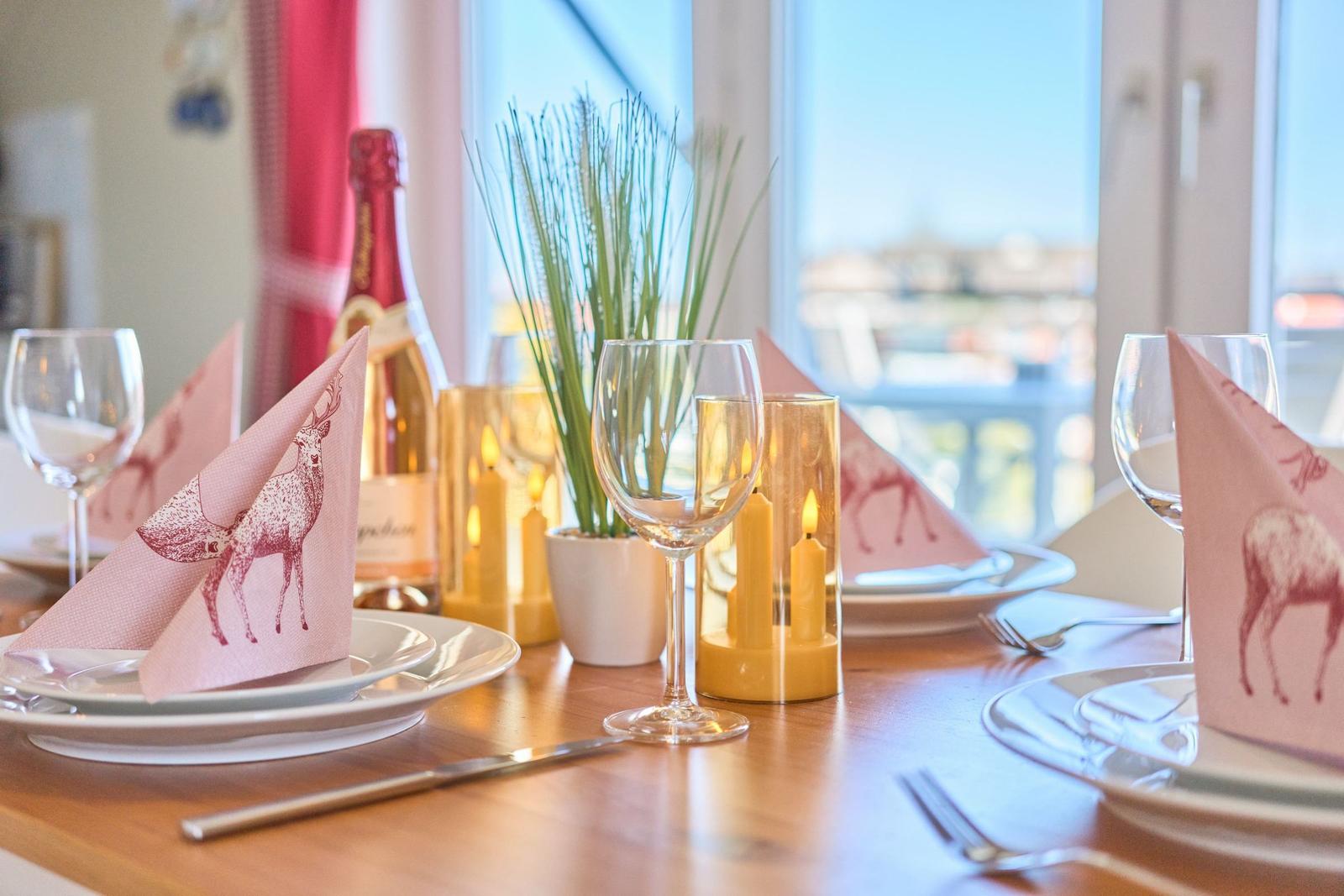 Gedeckter Tisch mit rosa Servietten, Gläsern und Kerzen. Blick auf Balkon mit Blick auf Wasser.