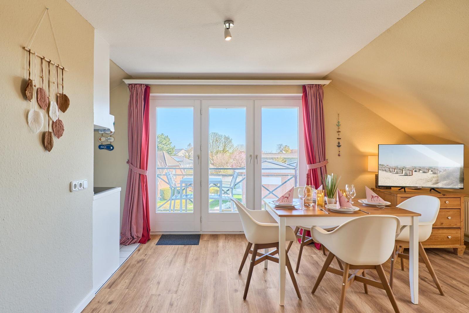 Esszimmer mit Tisch, Stühlen und Balkontür. Fernseher und Wohnbereich sichtbar.