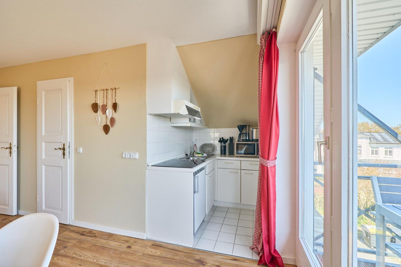 Küche mit weißen Schränken, Herd und Fenster zur Terrasse.