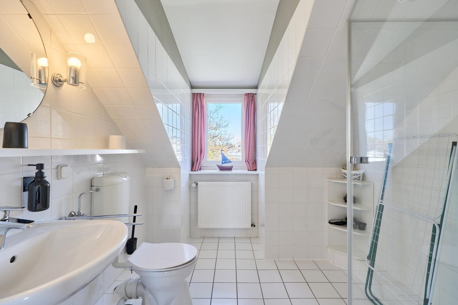 Badezimmer mit Dusche, Toilette und Waschbecken unter Dachschräge.
