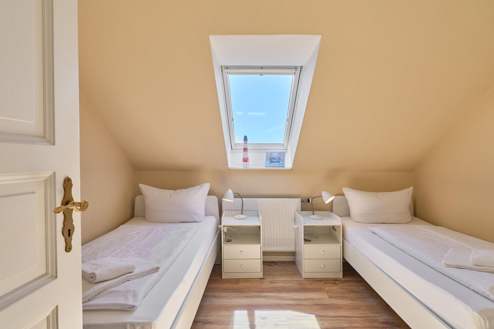Zwei Einzelbetten unter Dachschräge mit Dachfenster und Nachttischen.