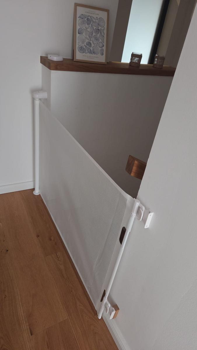Weißes Babygitter an Wand, Holzregal mit Bild und Kerzen darüber.