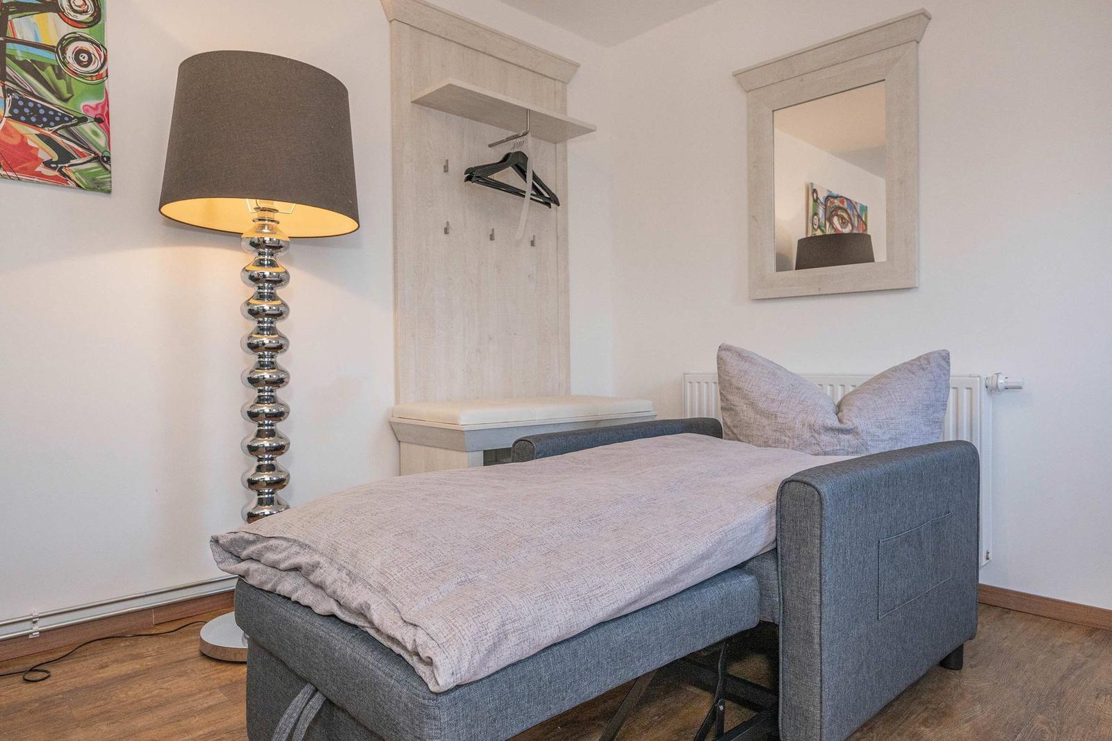 Schlafzimmer mit Bett, Kleiderhaken und Spiegel an der Wand.