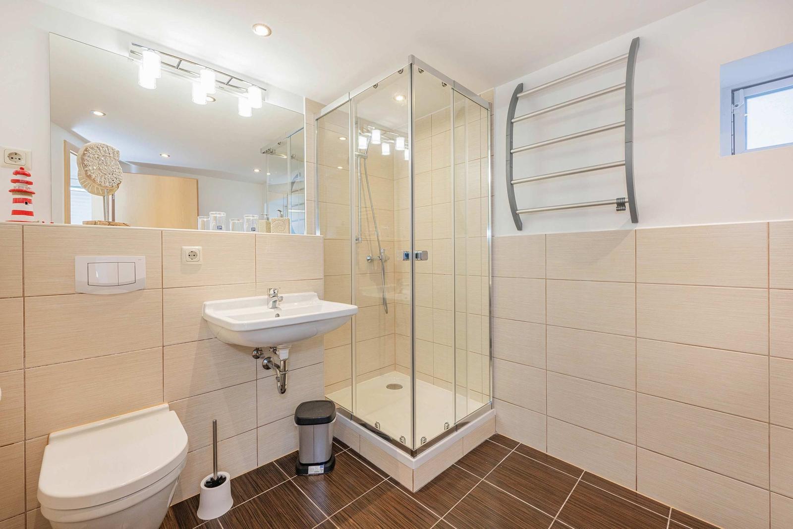Badezimmer mit Dusche, Waschbecken und Toilette. Fliesenwand und Holzfußboden.