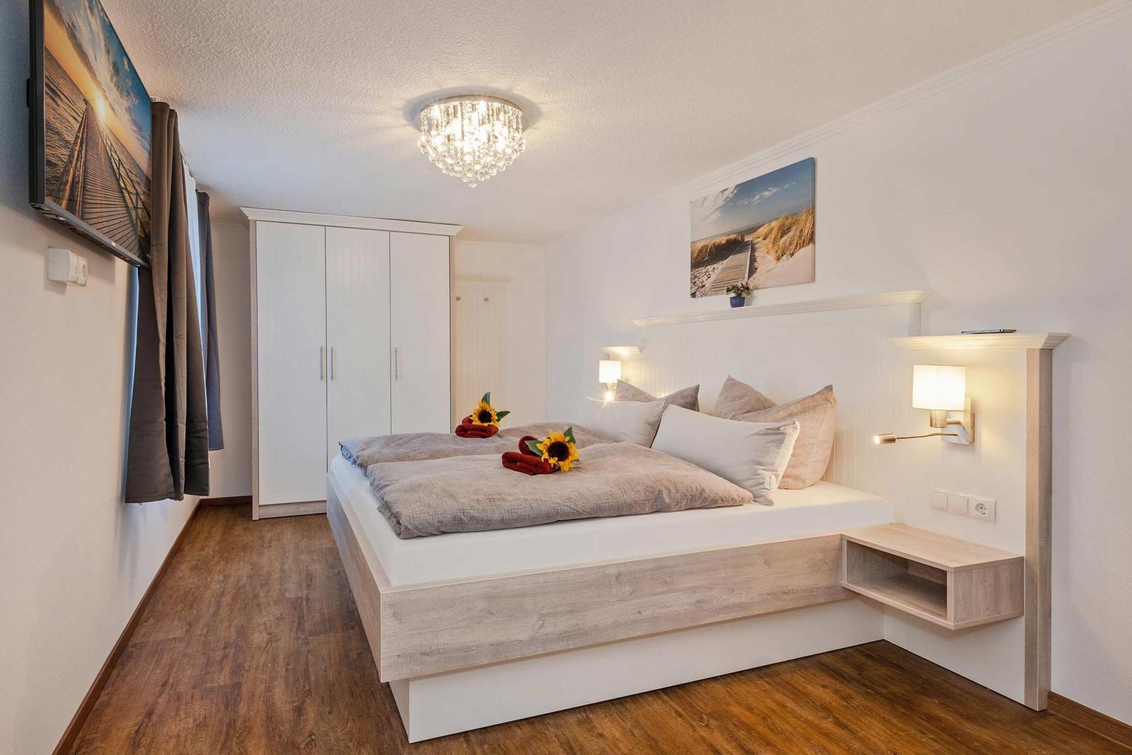 Schlafzimmer mit Bett, Kleiderschrank und Wandbild. Deckenleuchte und Nachttische.