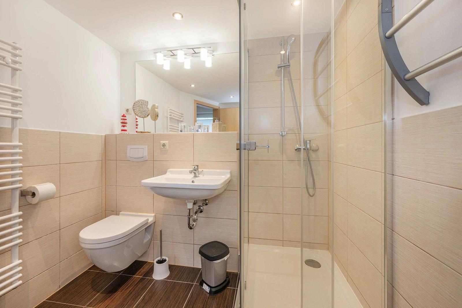 Bad mit Dusche, Waschbecken und Toilette. Holzoptik und weiße Fliesen.