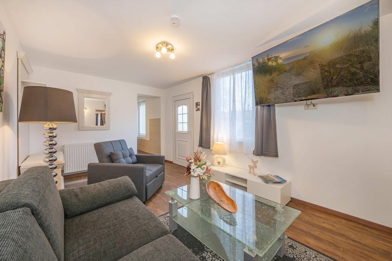 Wohnzimmer mit Sofa, Couch, Glas-Tisch und Fernseher an der Wand.