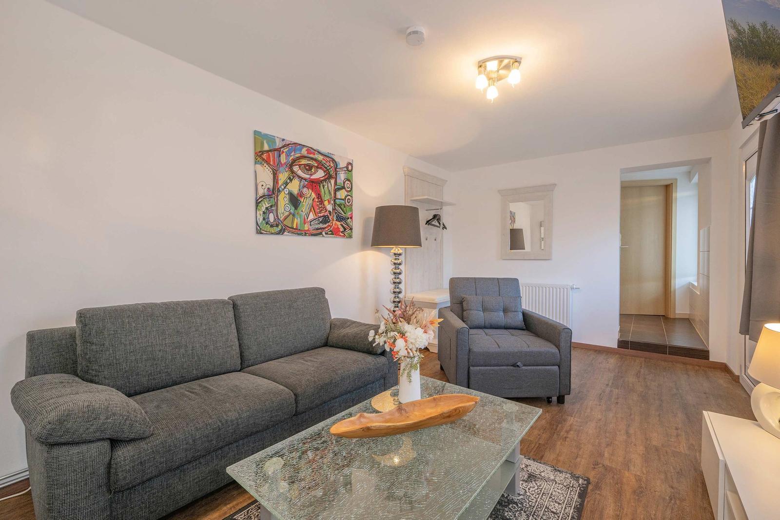 Wohnzimmer mit grauem Sofa, Glas-Tisch und Wandbild.