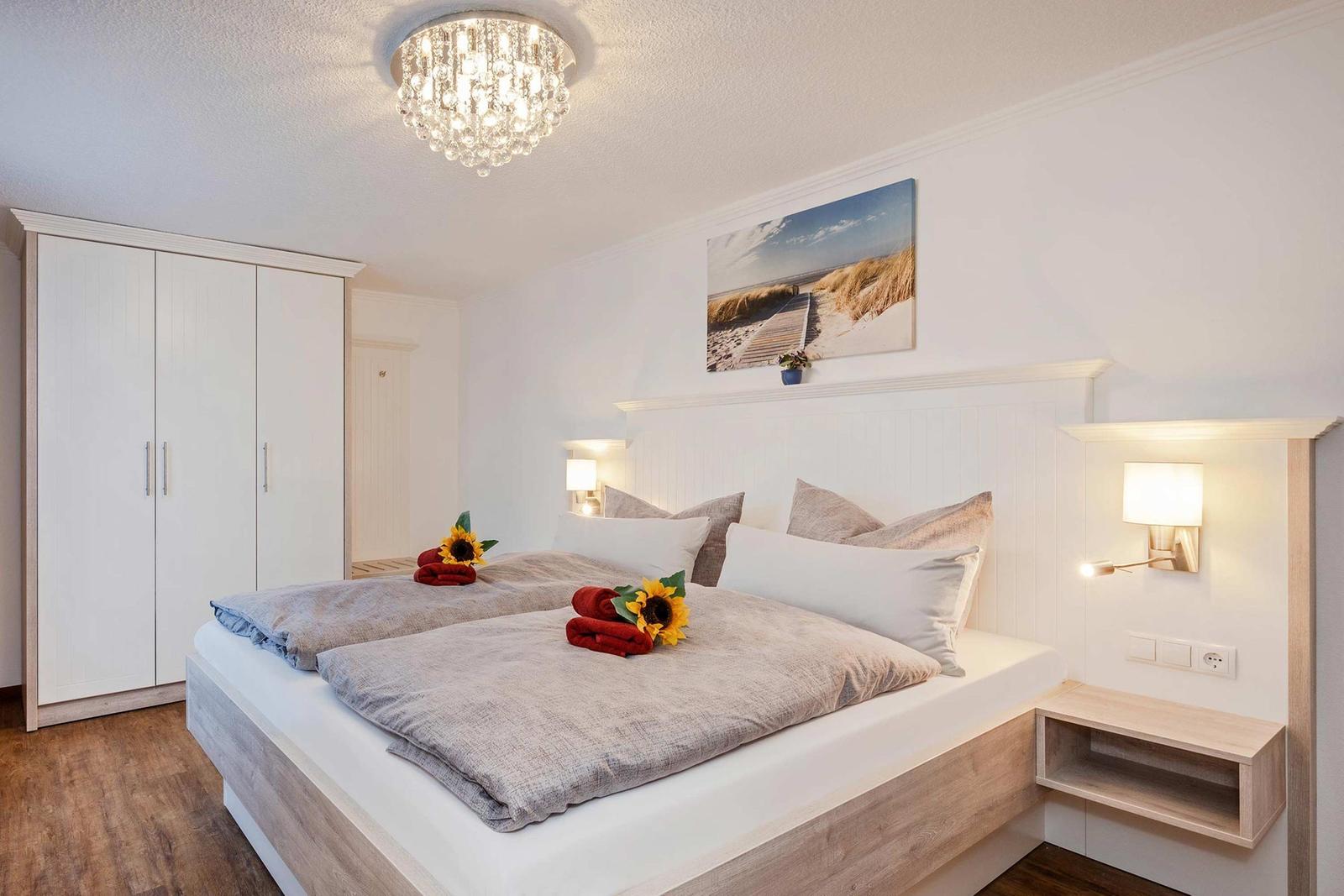 Schlafzimmer mit Doppelbett, Kleiderschrank und Wandbild. Deckenleuchte und Nachttische.