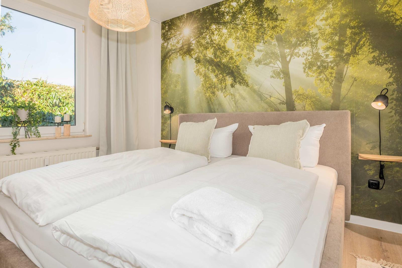 Schlafzimmer mit Bett, Fenster und Waldwandtapete.
