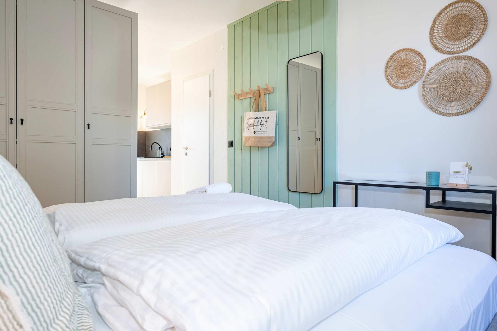 Schlafzimmer mit Bett, Kleiderschrank und grünem Wandpaneel mit Spiegel und Wanddekoration.