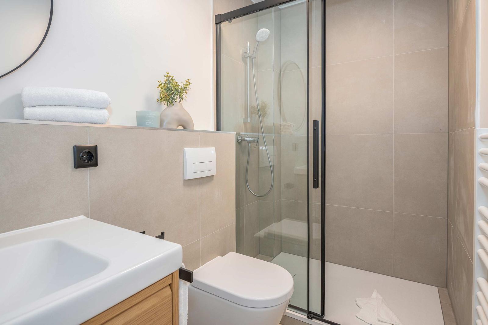 Badezimmer mit Dusche, Waschbecken und Toilette. Fliesen und moderne Ausstattung.