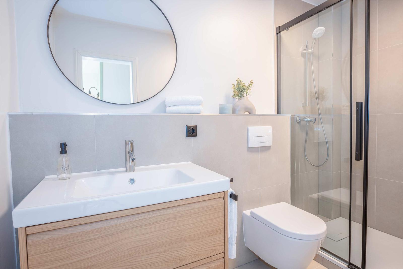 Bad mit Dusche, Waschbecken und Toilette. Runder Spiegel und Holzschrank.