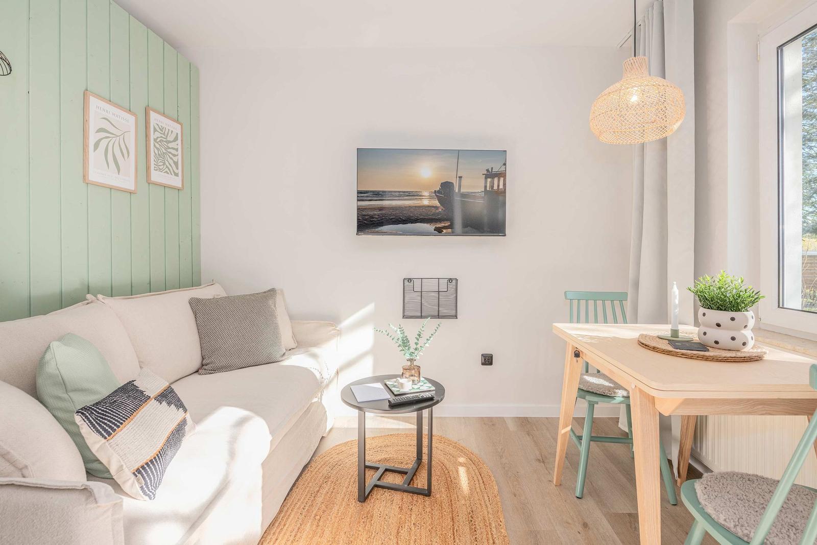 Wohn- und Essbereich mit Sofa, Tisch und Wandbild. Grüne Wand und Holzboden.